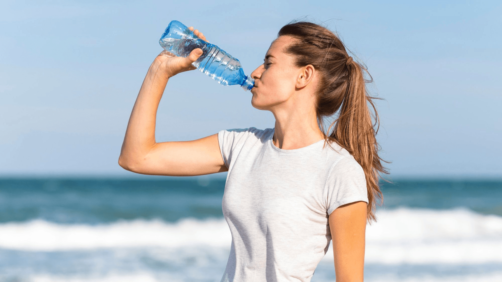 A girl drinking water at a beachside, promoting hydration and oral health awareness by a Glendale dentist