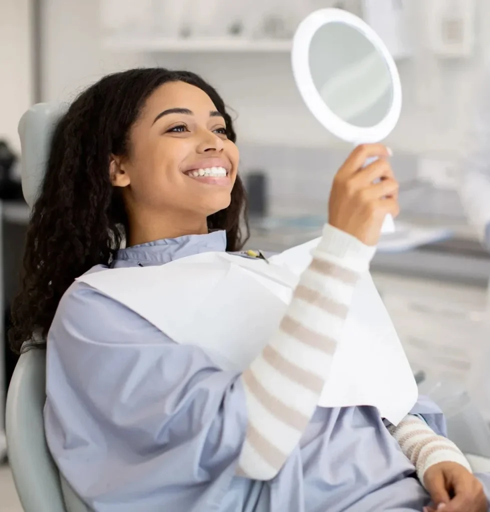 Smiling patient checking her new smile in a hand mirror at a cosmetic dentist in Glendale, AZ